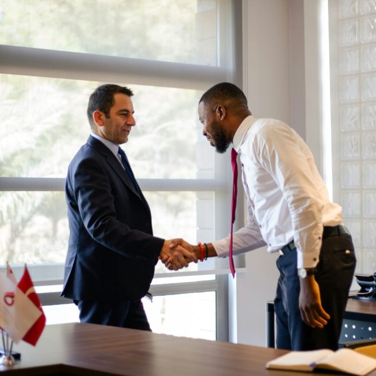 Partnerships Group of five people in formal attire engaging in conversation with drinks.